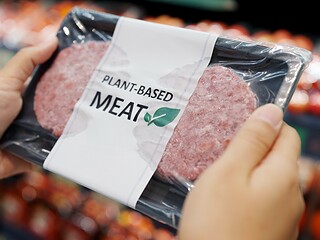 Hand greift im Supermarkt zu einer Packung pflanzlichem Fleischersatz mit der Aufschrift Plant-based Meat