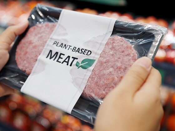 Hand greift im Supermarkt zu einer Packung pflanzlichem Fleischersatz mit der Aufschrift Plant-based Meat