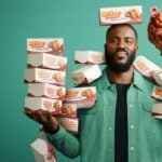 Big Chicken auf Netflix: 28 Tage Hähnchen, und ein Film, der zu früh bremst Mo Gilligan steht vor grünem Hintergrund mit Stapeln von Fried-Chicken-Boxen in den Händen, auf seiner Schulter sitzt ein Huhn