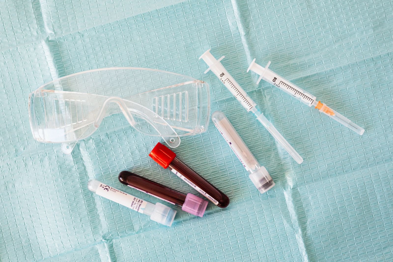 Blood collection tubes and syringes on a green laboratory surface