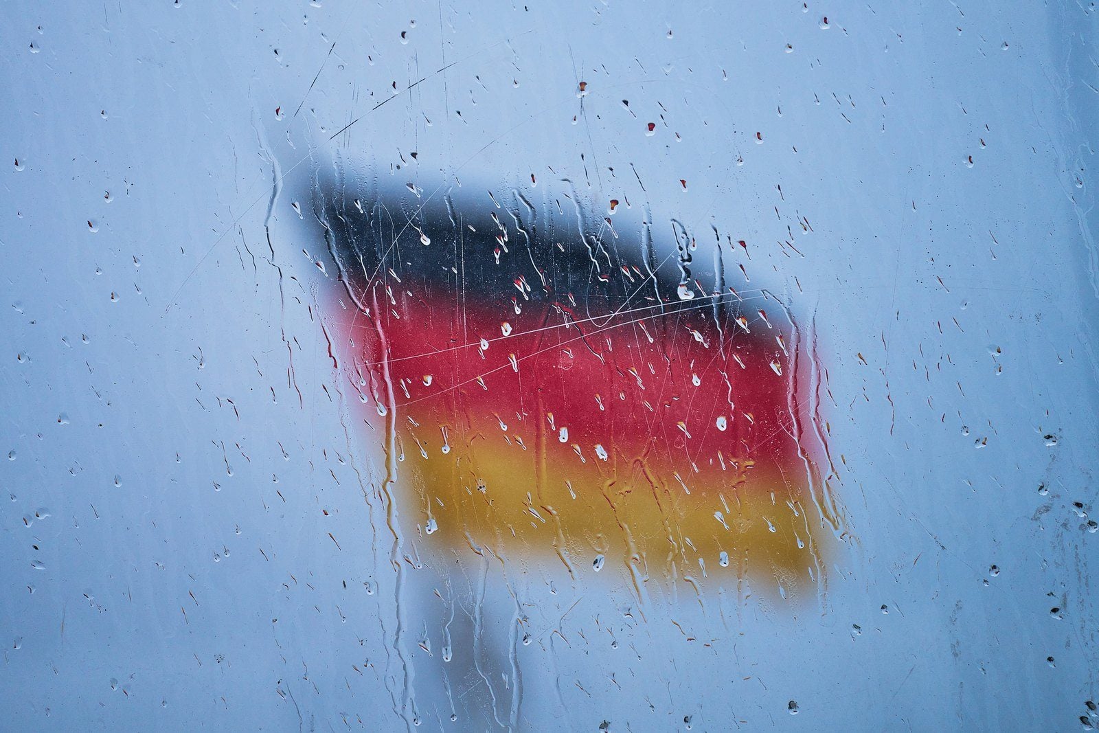 Deutschlandfahne, unscharf hinter einer regennassen Fensterscheibe