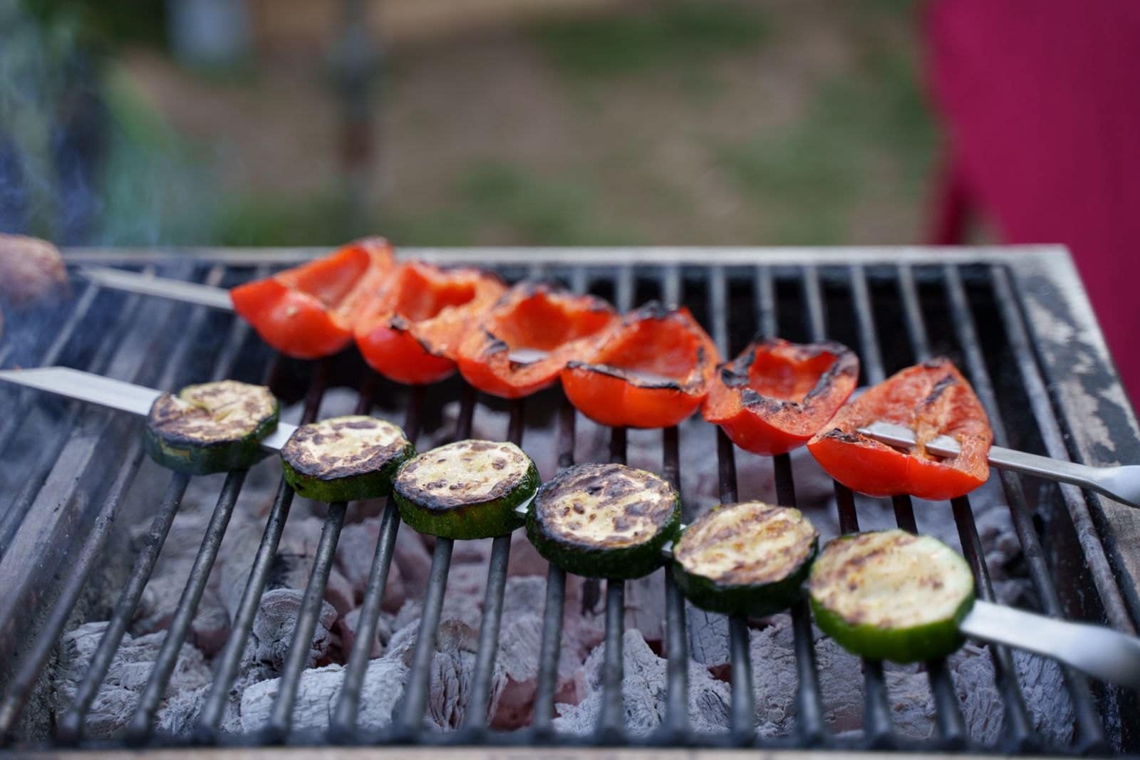 Spieße mit Zucchinischeiben und Paprikastücken liegen über der Glut