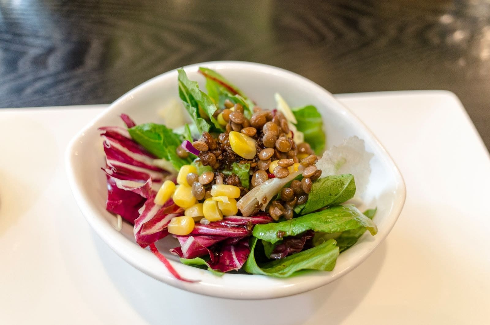 Schüssel mit Linsensalat, Mais und Blattsalat auf dunklem Holztisch