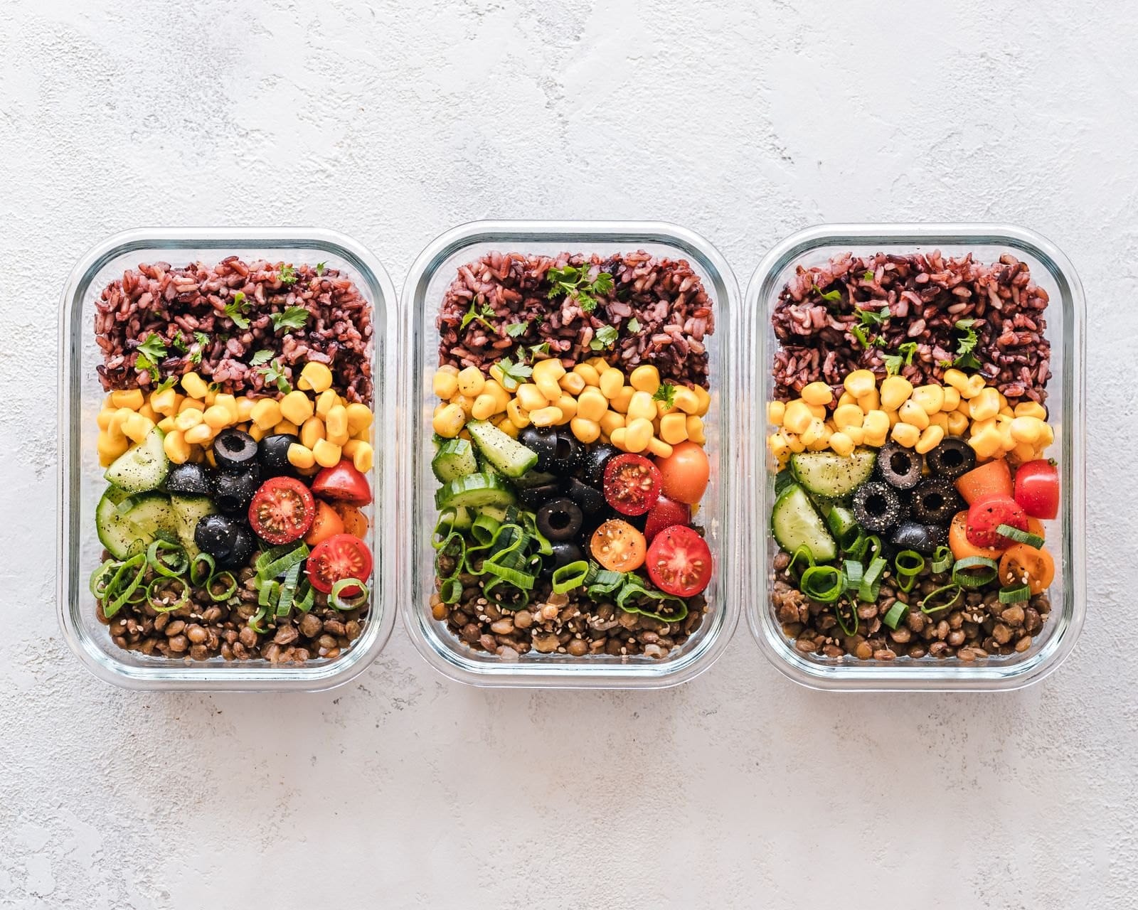 Drei Meal-Prep-Boxen mit Reis, Kichererbsen, Tomaten und Gemüse von oben fotografiert