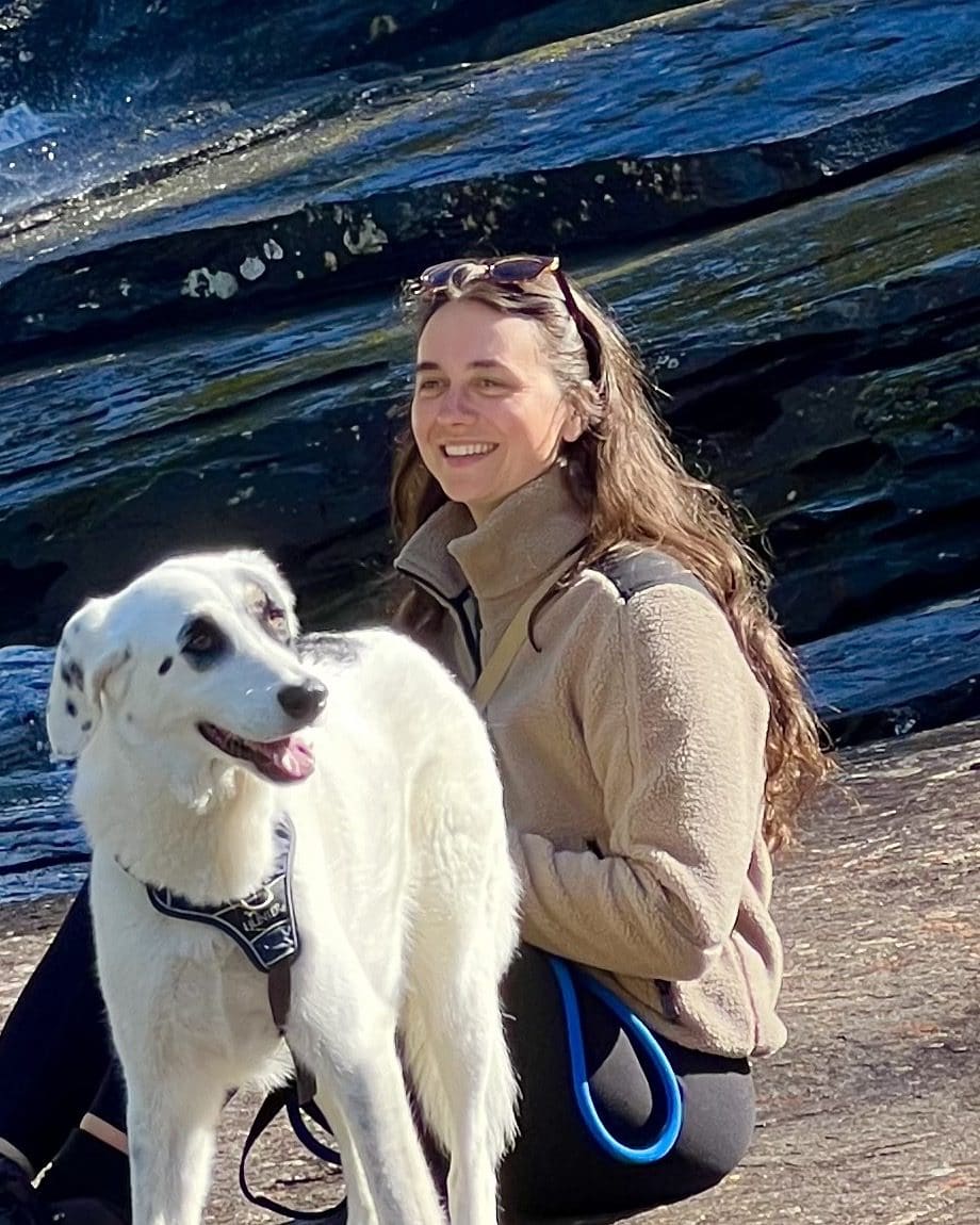 Milena Röver, Ernährungswissenschaftlerin B.Sc. bei This Is Vegan, sitzt mit ihrem weißen Hund auf einem Felsen in der Natur