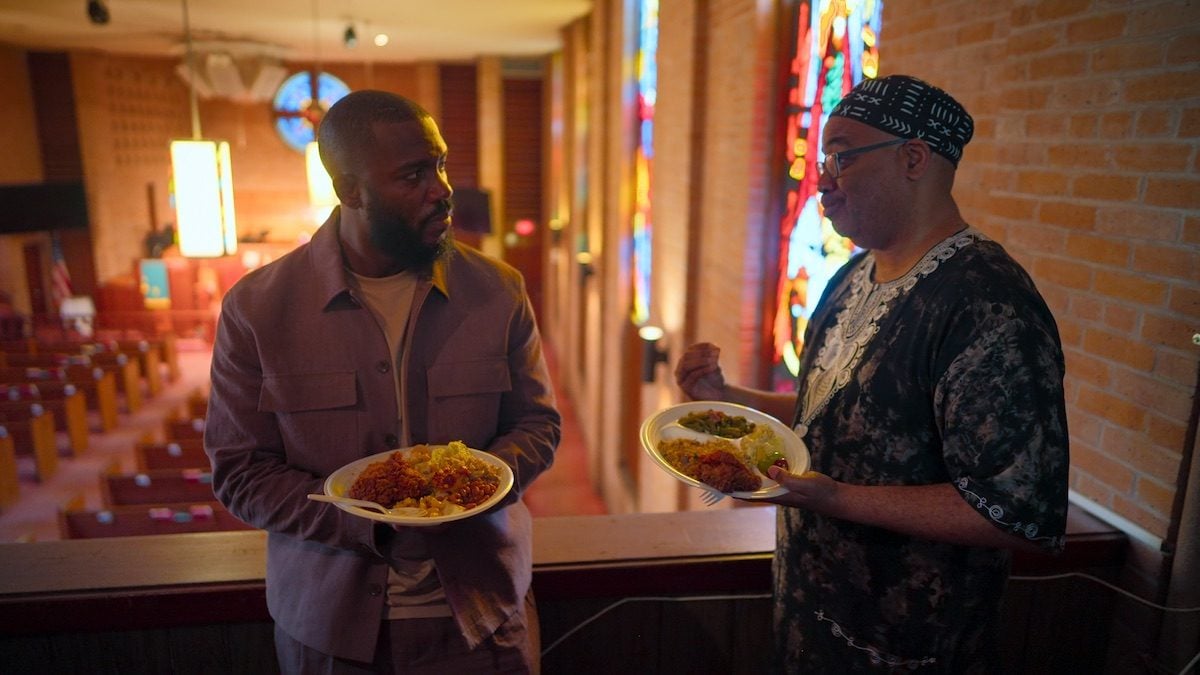 Mo Gilligan im Gespräch mit einem Mann in einer Kirche, beide halten Teller mit Essen in den Händen