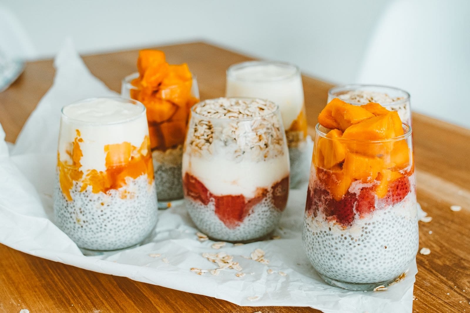 Drei Glaeser mit Overnight Oats und Chiapudding, geschichtet mit Mango und Beeren