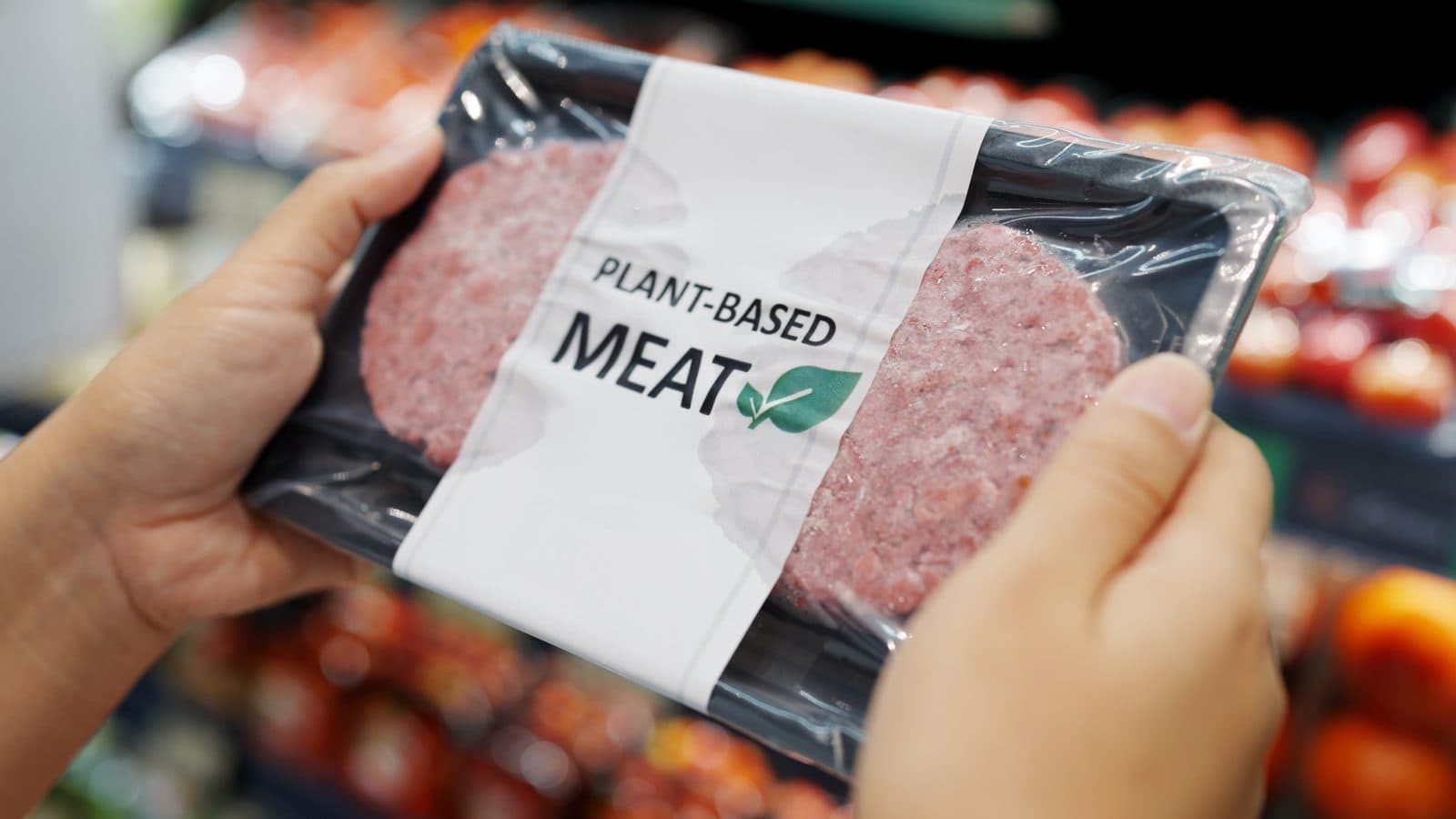 Hands lifting a packaged tray of plant-based mince labelled Plant-Based Meat from a supermarket shelf