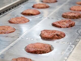 Pflanzliche Steaks von Planted liegen in Reihen auf einem Produktionsband
