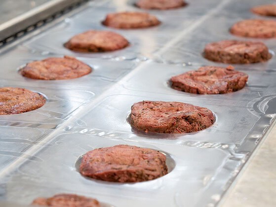 Pflanzliche Steaks von Planted liegen in Reihen auf einem Produktionsband