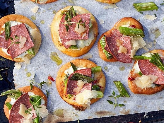 Cracker mit Scheiben veganer Salami, Frühlingszwiebeln und Kräutern auf einem Backblech