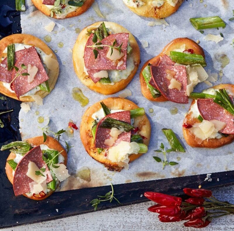 Cracker mit Scheiben veganer Salami, Frühlingszwiebeln und Kräutern auf einem Backblech