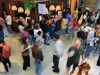 Viele Menschen mit grünen Lanyards im Café- und Netzwerkbereich des SFT Festivals, teils in Bewegungsunschärfe