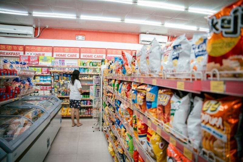 Woman standing at the end of a supermarket aisle lined with shelves of packaged food