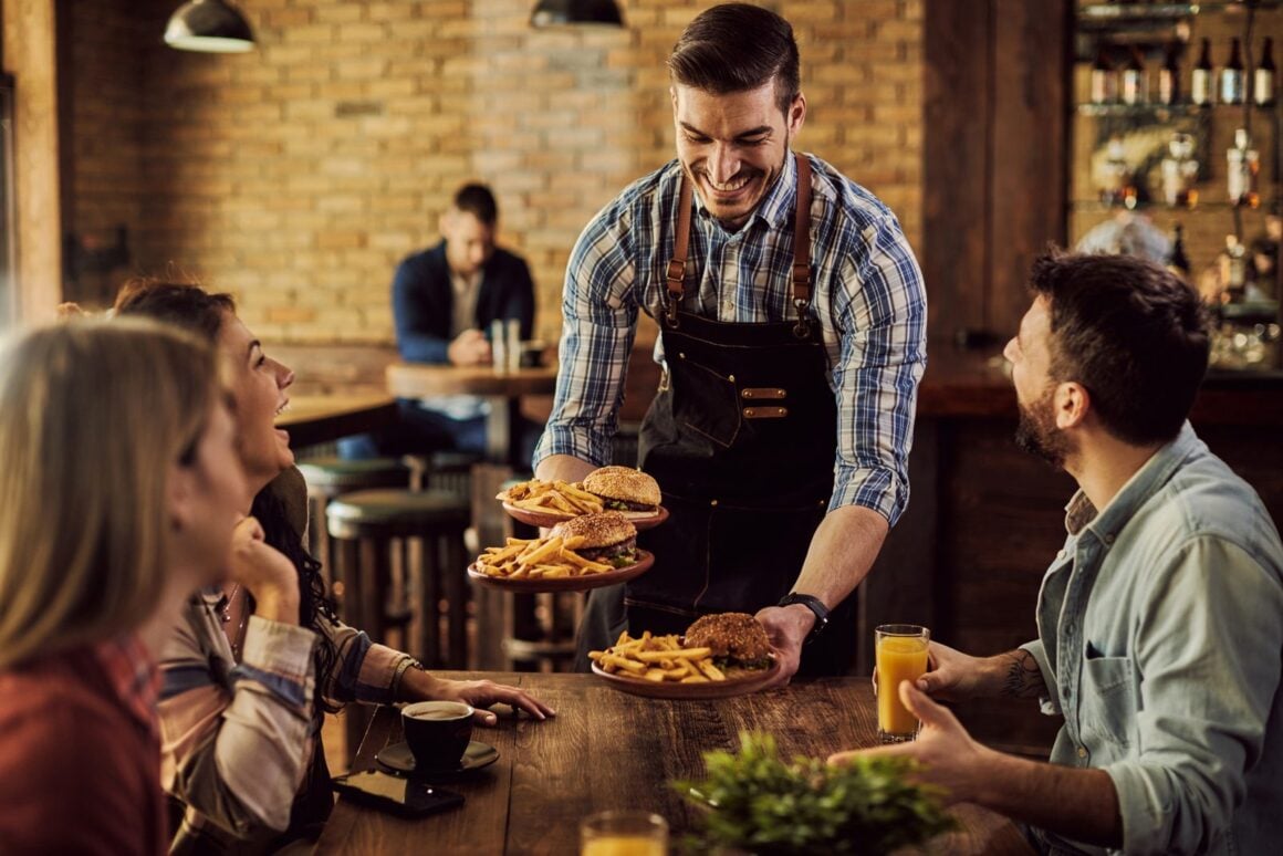 Kellner serviert Essen an einen Tisch mit fröhlicher Gruppe in einem Pub