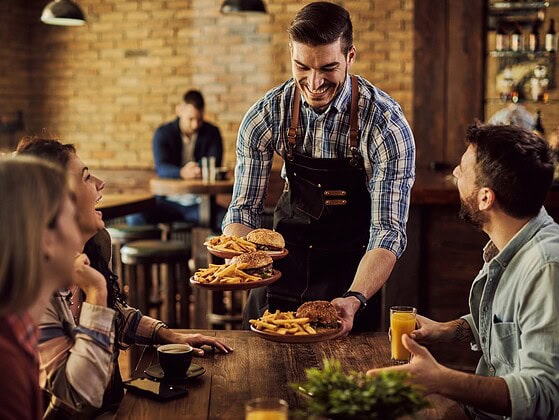 Kellner serviert Essen an einen Tisch mit fröhlicher Gruppe in einem Pub