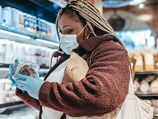Frau steht im Supermarkt und liest die Rückseite einer Lebensmittelverpackung
