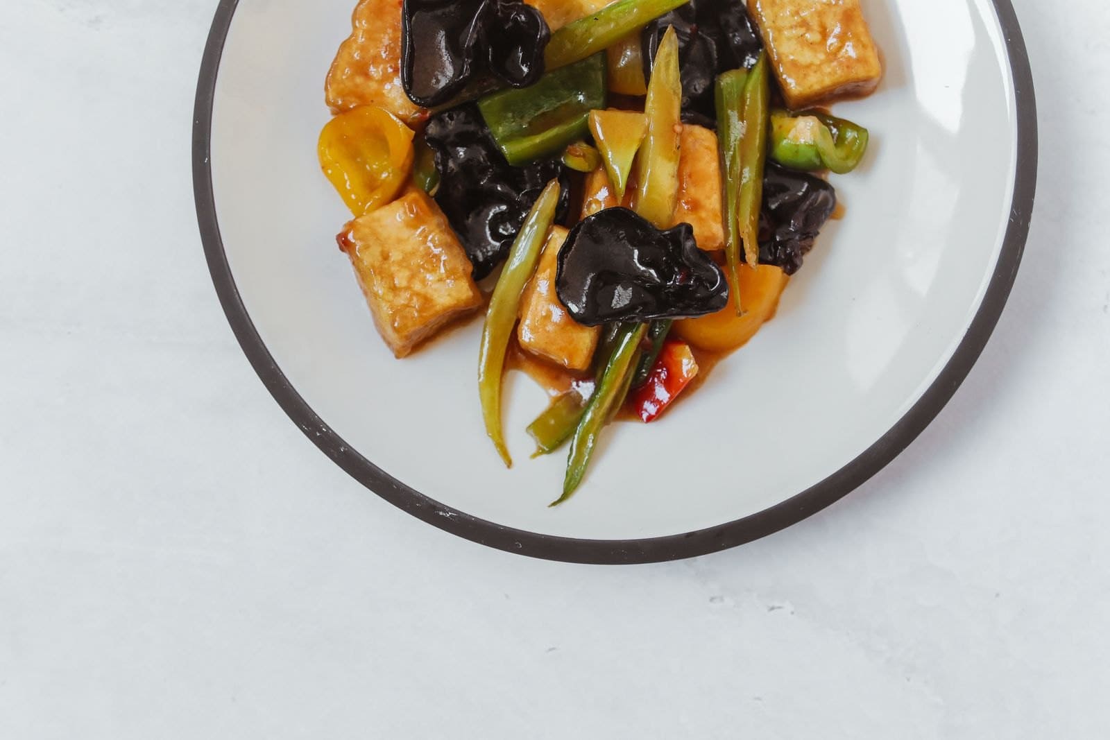 Gebratene Tofuwürfel mit Paprika, Frühlingszwiebeln und Mu-Err-Pilzen auf einem Teller