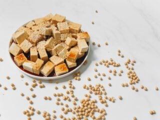 Tofuwürfel mit Sojasauce und Sesam auf einem Teller, daneben verstreute Sojabohnen