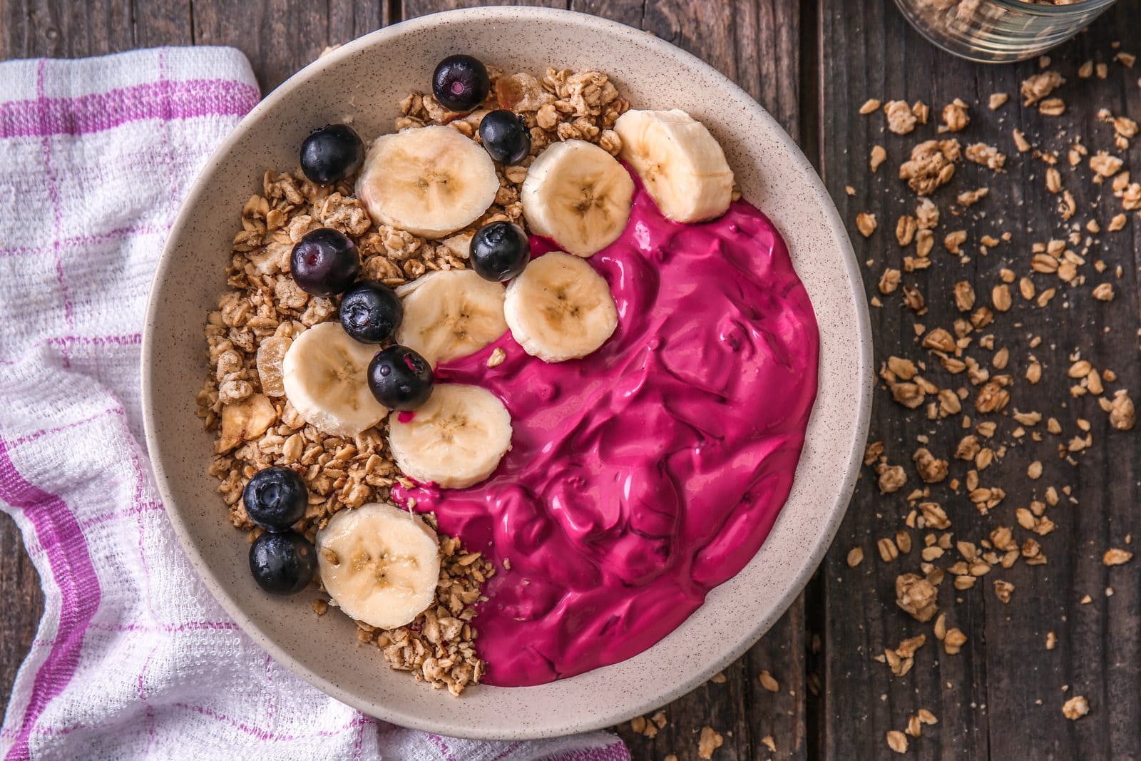 Smoothie-Bowl mit Beeren, Bananenscheiben, Heidelbeeren und Granola auf Holztisch