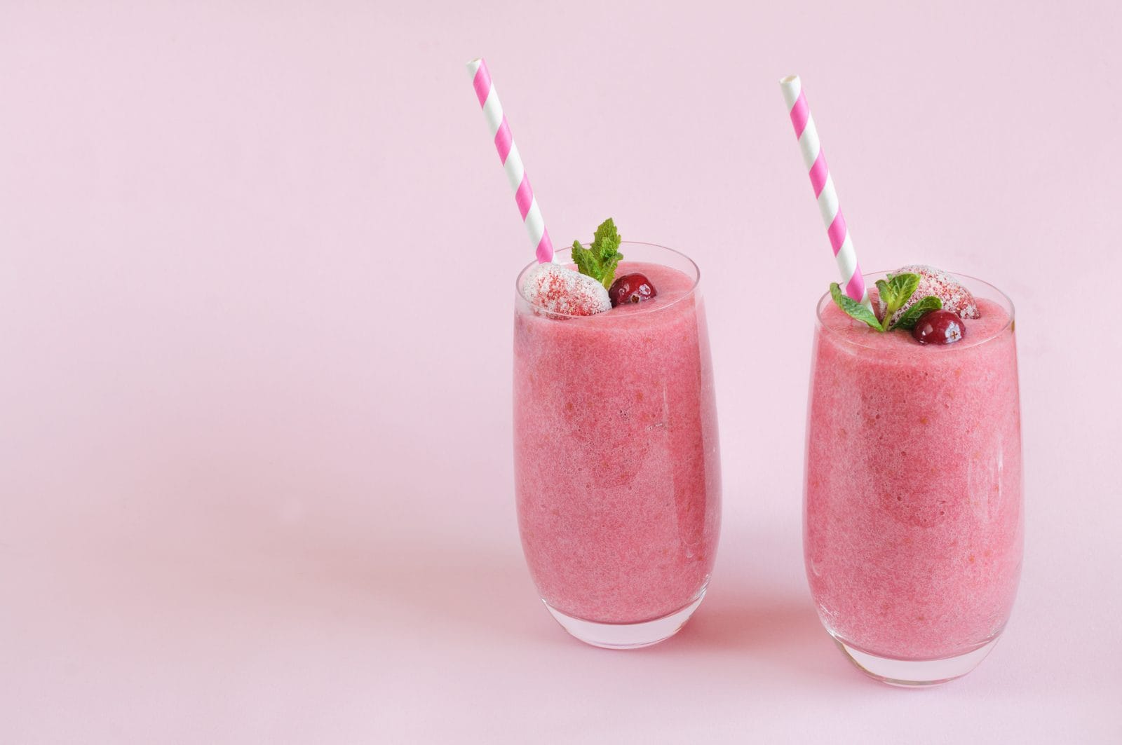 Zwei rosa Beeren-Smoothies mit Minze und Papier-Strohhalmen