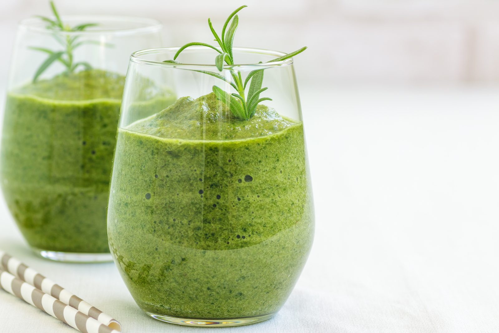 Zwei Glaeser gruener Smoothie mit Spinat, garniert mit Rosmarin