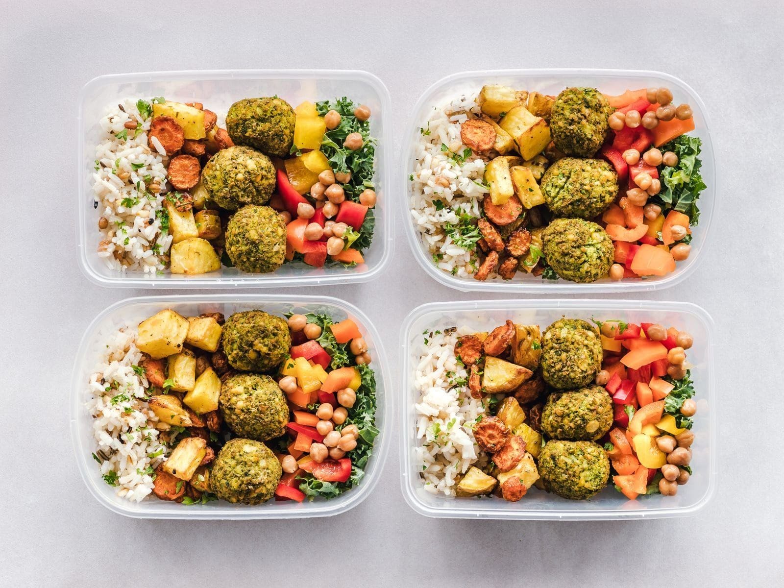 Vier vorbereitete Meal-Prep-Boxen mit Falafel, Reis und Gemüse nebeneinander