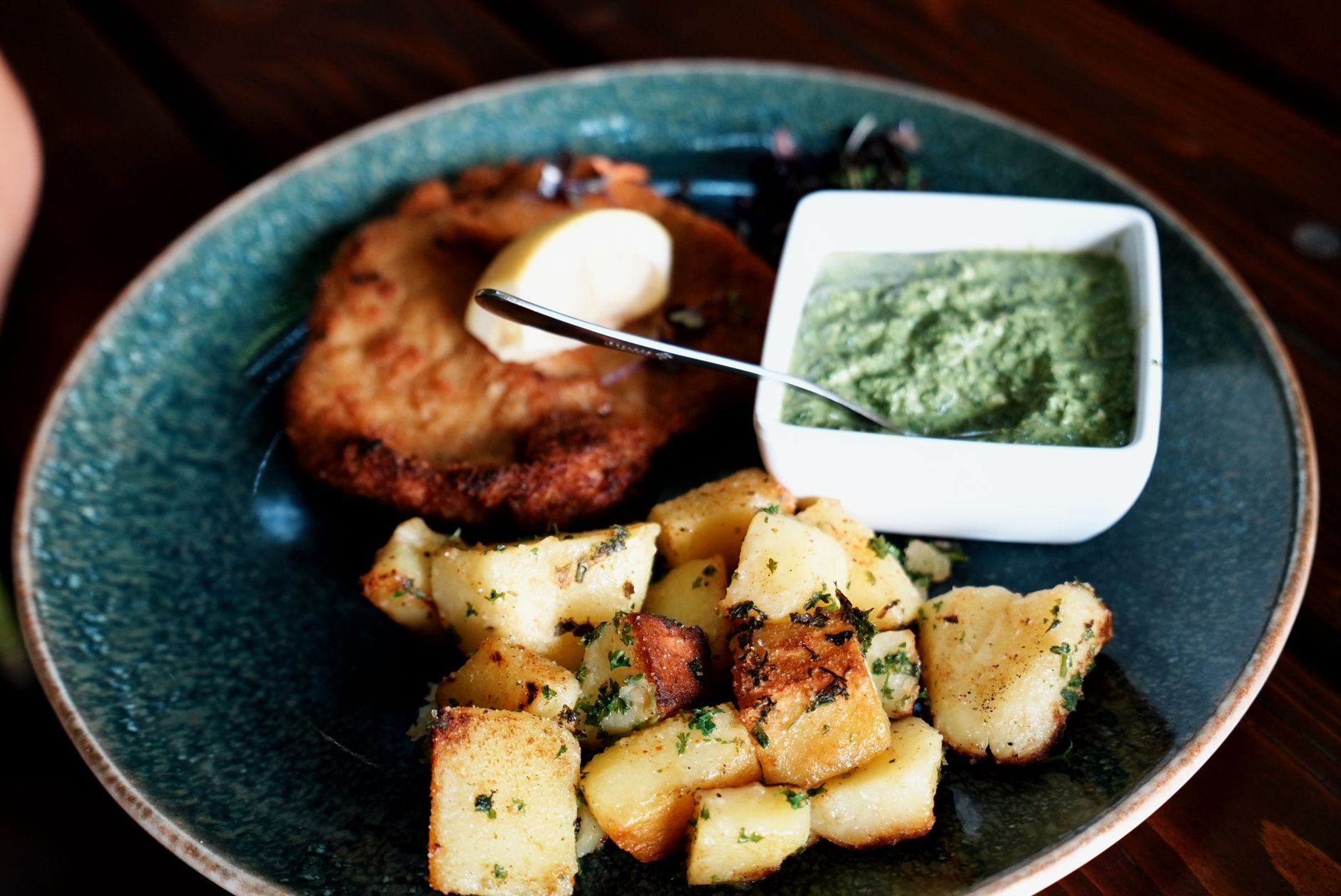 Paniertes Schnitzel mit Bratkartoffeln und gruener Sauce auf blauem Teller