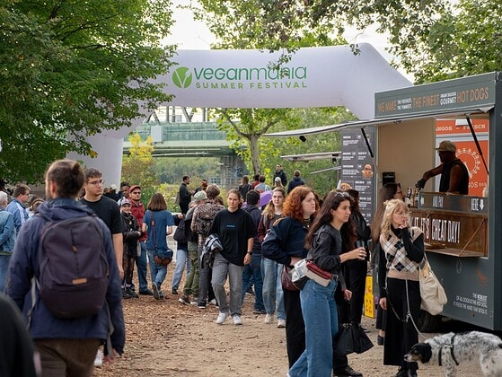 Eingangsbogen der VeganMania Summer Festival auf der Donauinsel Wien mit Besucherinnen und Besuchern und Foodtruck