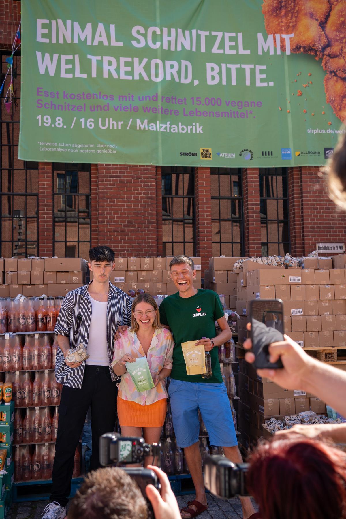 Banner mit der Aufschrift Einmal Schnitzel mit Weltrekord bitte vor Paletten mit geretteten Lebensmitteln