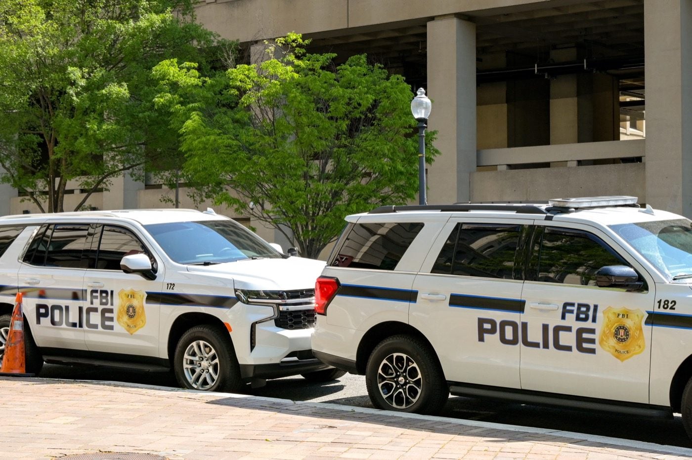 Zwei weiße Einsatzfahrzeuge mit der Aufschrift FBI Police vor einem Verwaltungsgebäude