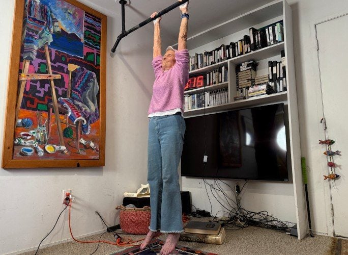 Ann Esselstyn hängt beim Rekordversuch an der Stange in ihrem Wohnzimmer, daneben die laufende Uhr