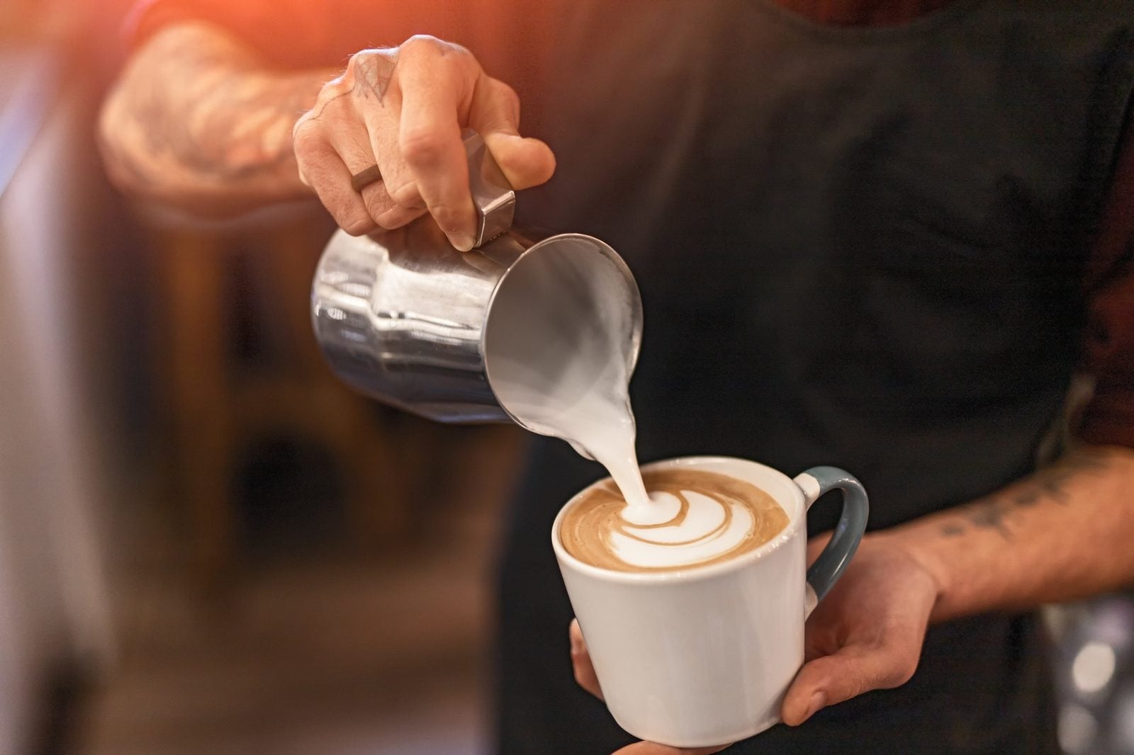 Barista gießt aufgeschäumte Milch für Latte Art in eine Tasse Cappuccino