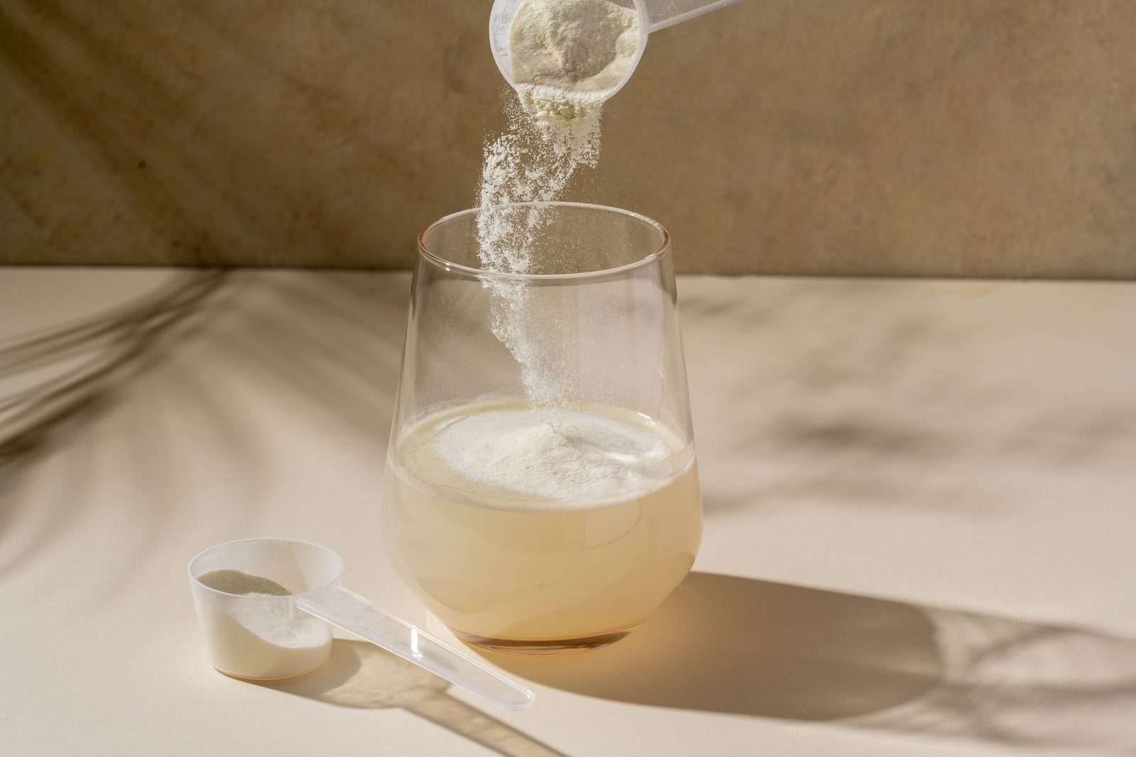 Weißes Pulver wird mit einem Messlöffel in ein Glas Wasser gegeben
