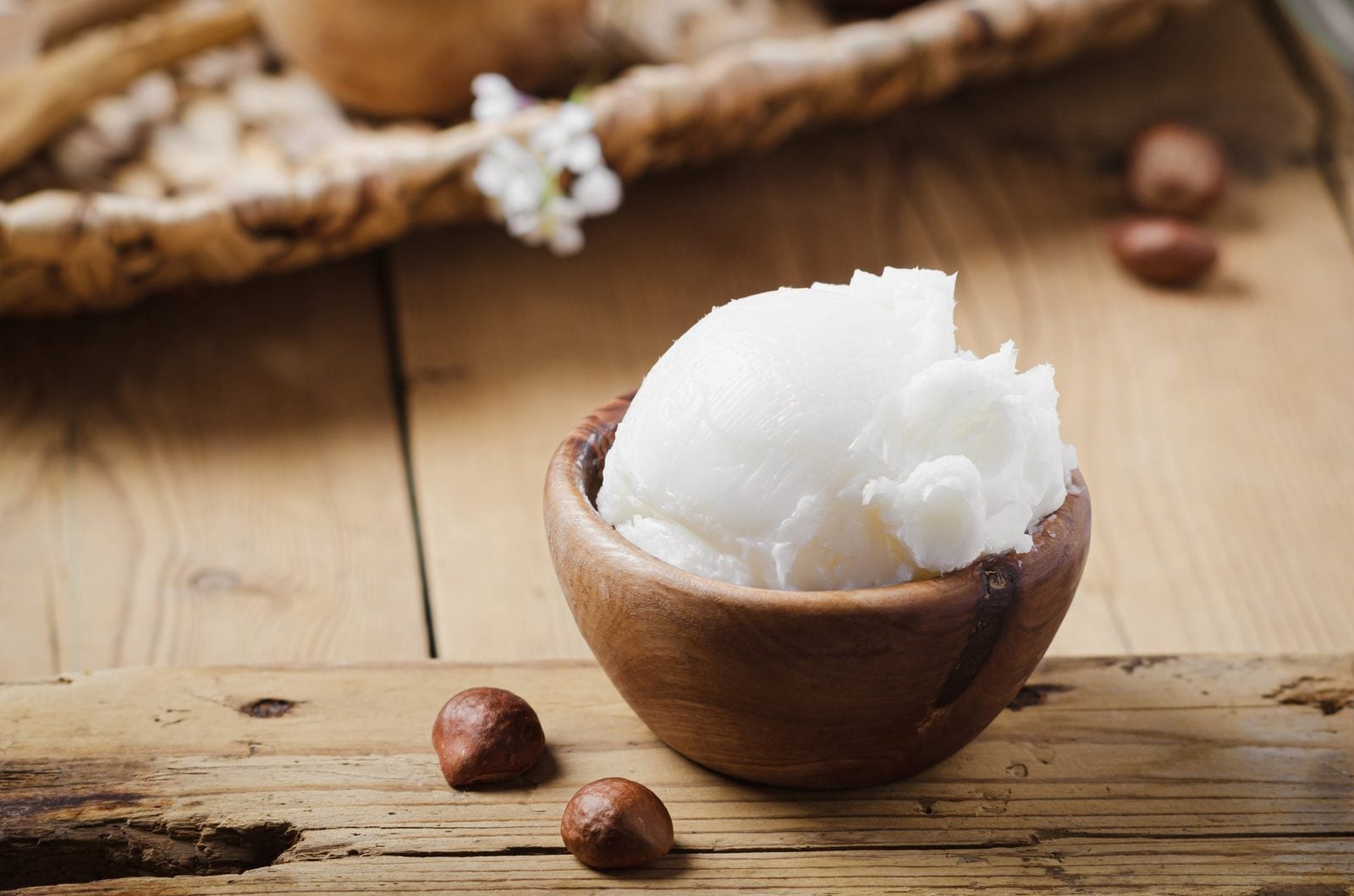 Unraffinierte Sheabutter in einer Holzschale, daneben Sheanüsse auf einem Holztisch