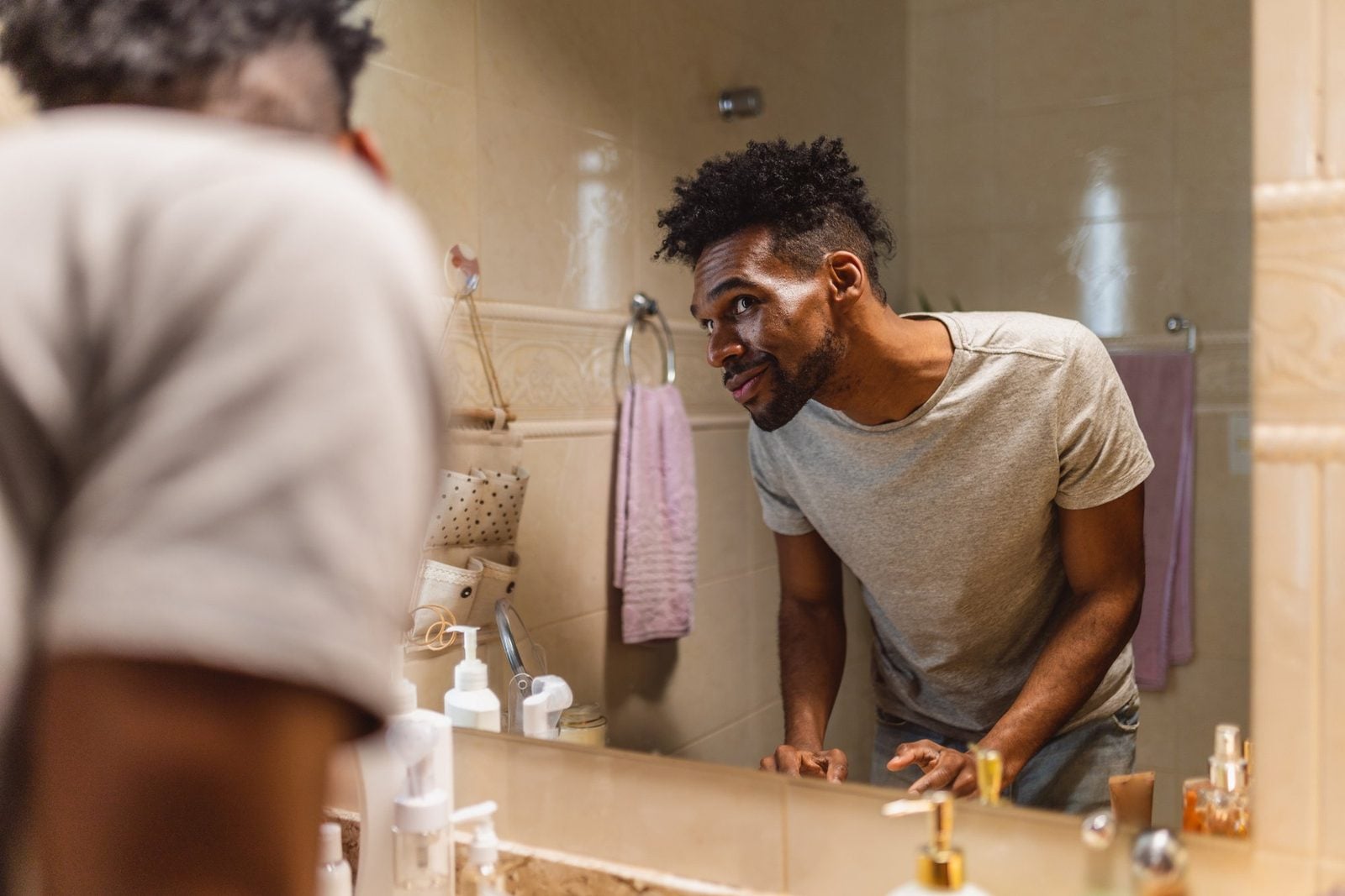 Mann steht morgens im Badezimmer vor dem Spiegel und betrachtet seine Haut