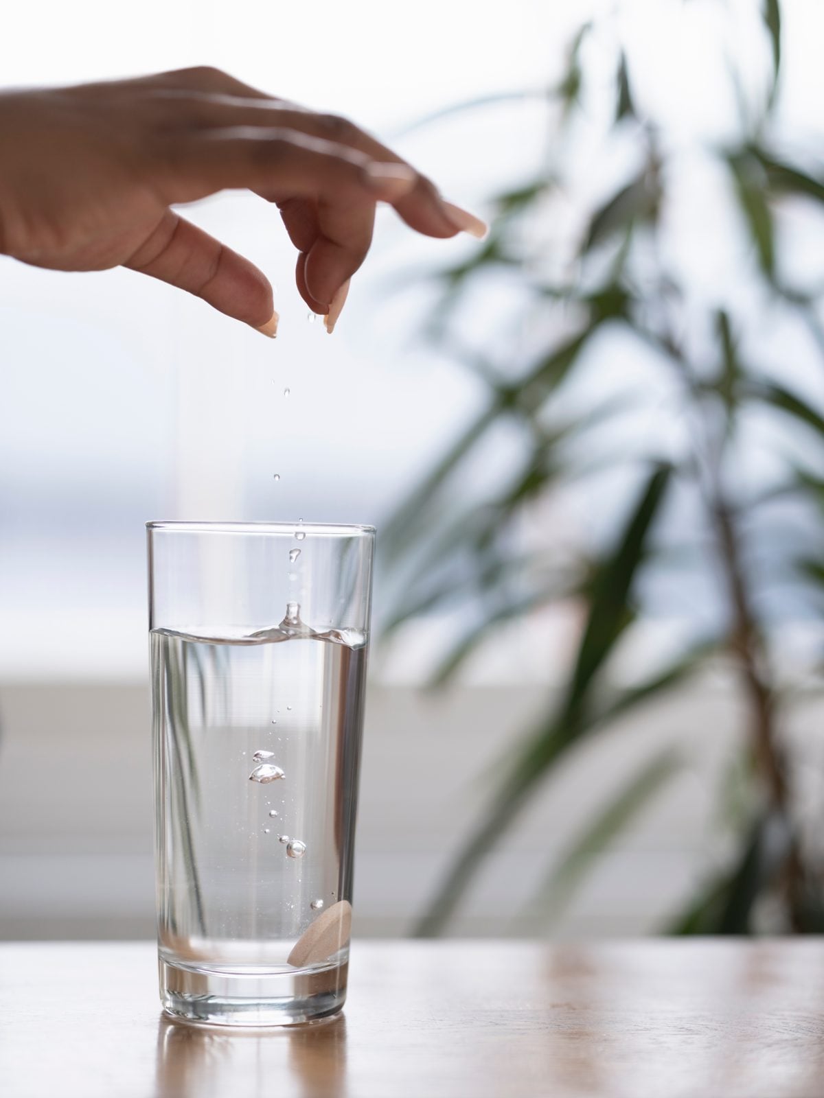 Hand lässt eine Brausetablette in ein Glas Wasser fallen