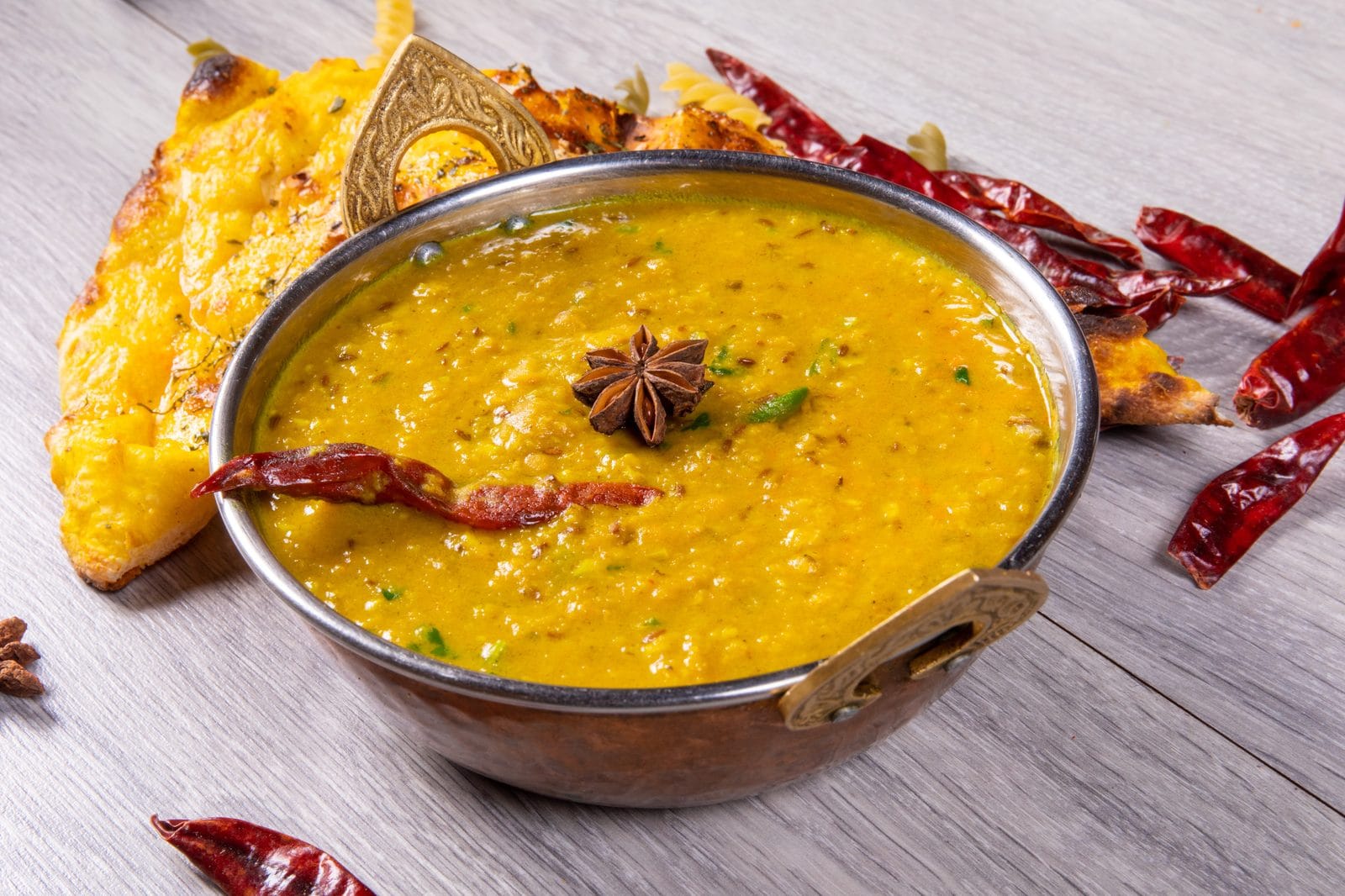 Dal Tadka in einer Kupferschale mit getrockneten Chilis und Sternanis, dazu ein Stück Fladenbrot