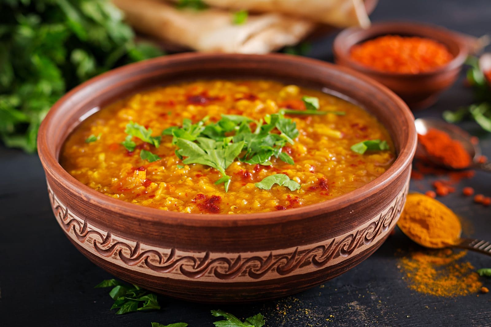 Gelbes Dal aus Linsen in einer Tonschale, garniert mit Koriander, daneben Gewürze und Chili