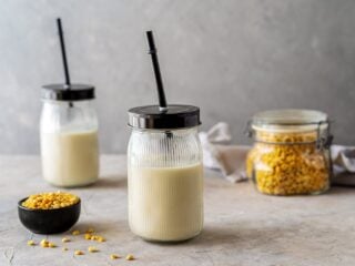 Erbsenmilch in zwei Gläsern mit Strohhalm, daneben getrocknete gelbe Erbsen