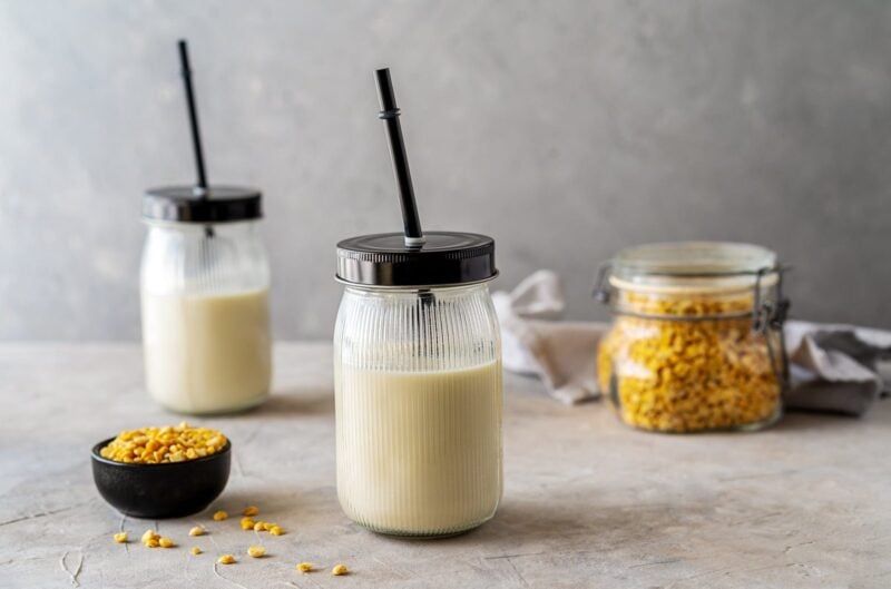 Erbsenmilch in zwei Gläsern mit Strohhalm, daneben getrocknete gelbe Erbsen