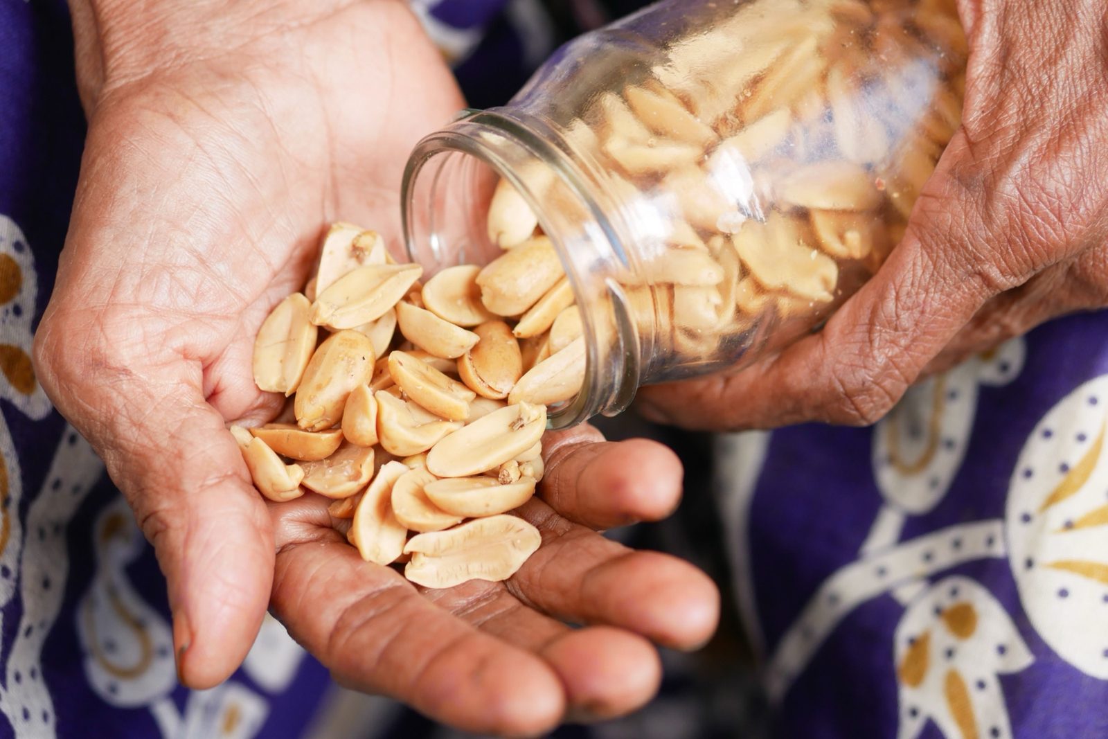 Hands pouring roasted, shelled peanuts from a glass jar into an open palm