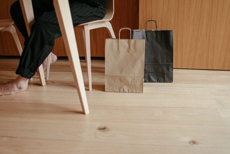 Zwei Einkaufstüten aus Papier stehen neben einem Stuhl auf dem Holzboden
