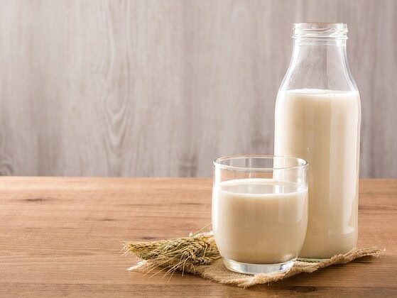 Hafermilch in Glas und Flasche auf einem Holztisch mit Haferähren