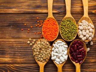 Verschiedene Hülsenfrüchte auf Holzlöffeln: rote Linsen, Mungbohnen, Kichererbsen, Kidneybohnen und weiße Bohnen