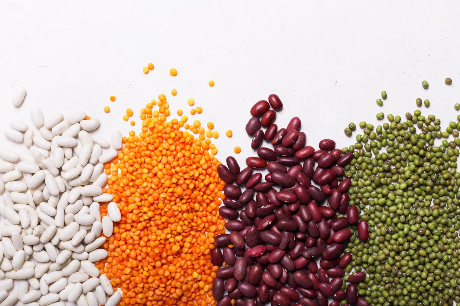Weiße Bohnen, rote Linsen, Kidneybohnen und Mungbohnen nebeneinander auf hellem Untergrund