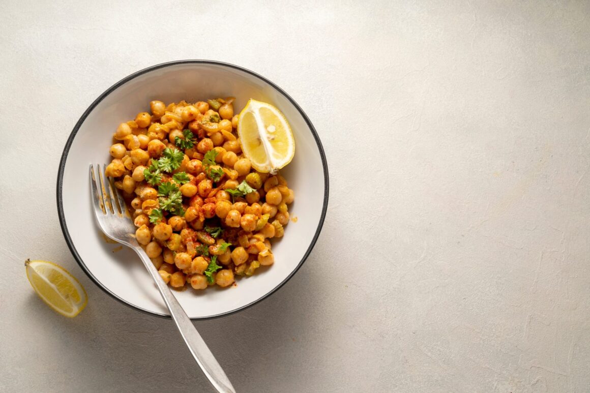 Veganes Kichererbsen-Curry mit Tomaten und Petersilie in einer weißen Schale, daneben Zitrone und Löffel