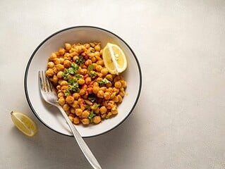 Veganes Kichererbsen-Curry mit Tomaten und Petersilie in einer weißen Schale, daneben Zitrone und Löffel