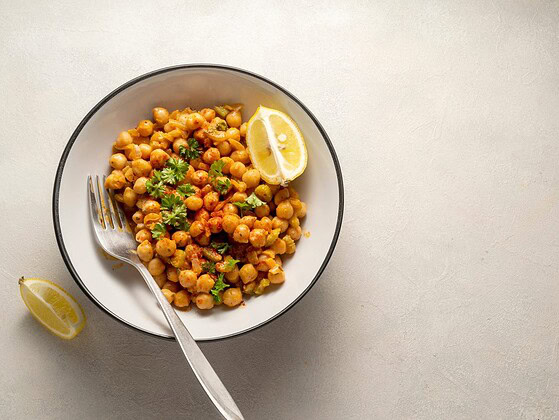 Veganes Kichererbsen-Curry mit Tomaten und Petersilie in einer weißen Schale, daneben Zitrone und Löffel