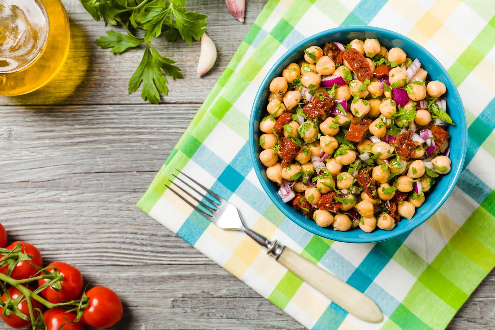 Kichererbsensalat mit getrockneten Tomaten, Zwiebel und Kräutern in einer Schüssel auf kariertem Tuch